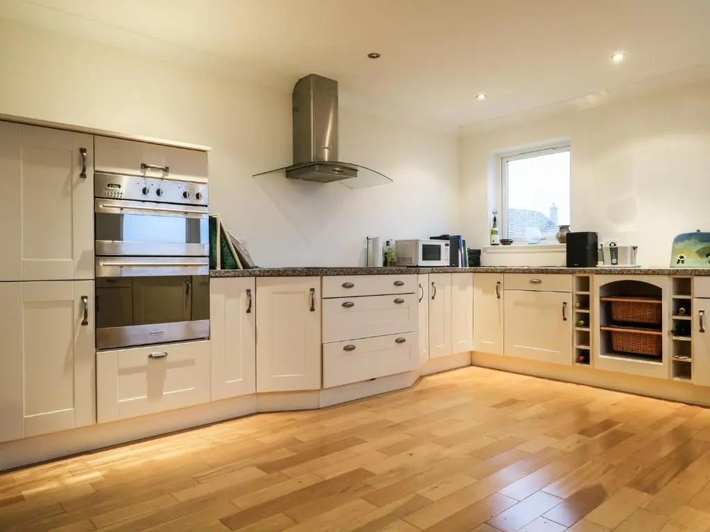 a kitchen with white cabinets and a wooden floor at Glaven in Bonar Bridge