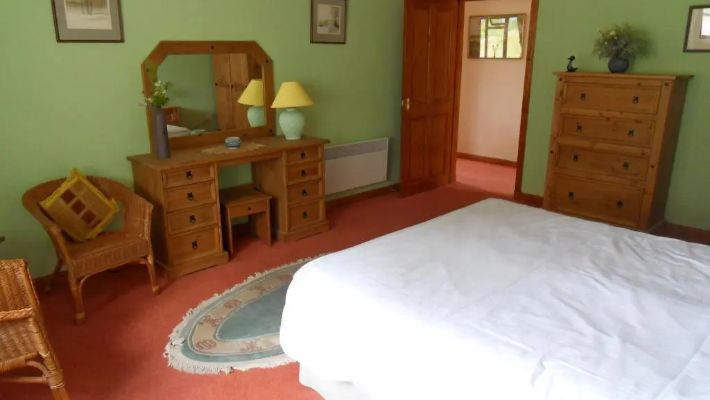 a bedroom with a bed and a dresser and a mirror at Meadowside Cottages in Balavil