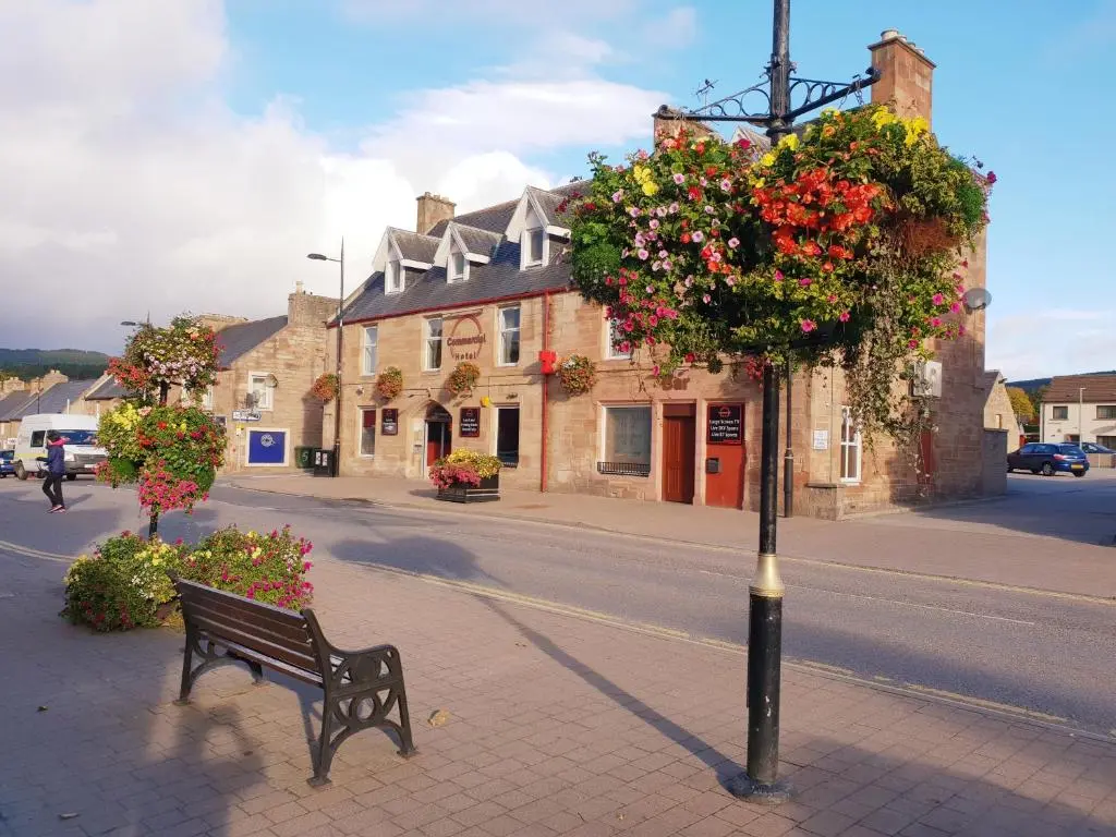a bench on a sidewalk next to a street with flowers at Commercial Hotel in Alness