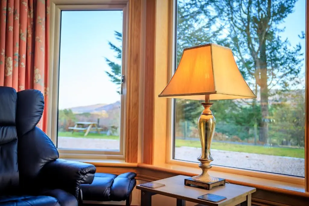 a lamp on a table next to a chair and a window at Crubenbeg Country House in Newtonmore