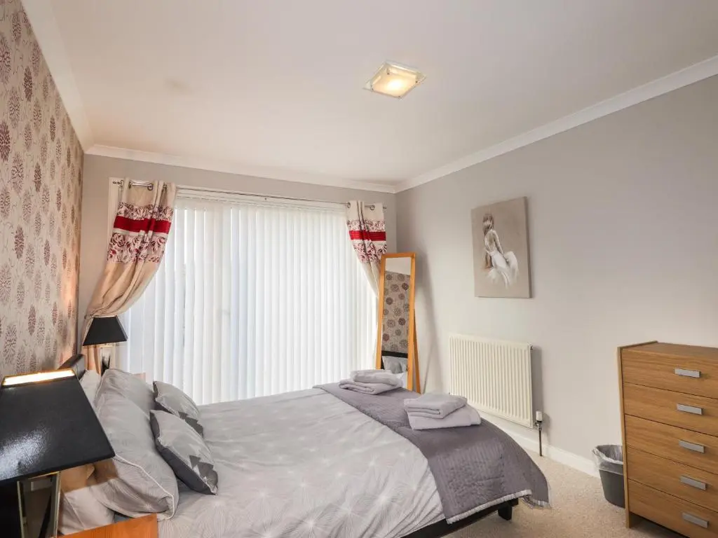 a bedroom with a bed and a dresser and a window at Rose Cottage in Lybster