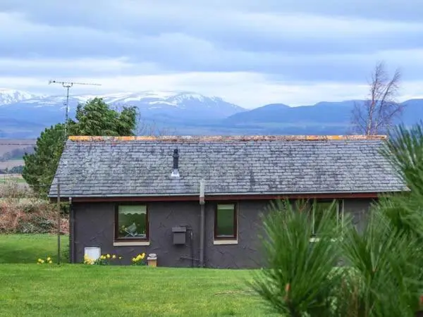 a small house in a field with mountains in the background at Pine Lodge in Resolis
