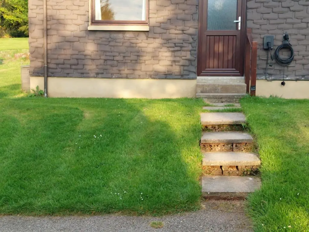 a house with a door and some stairs in the grass at Pine Lodge in Resolis