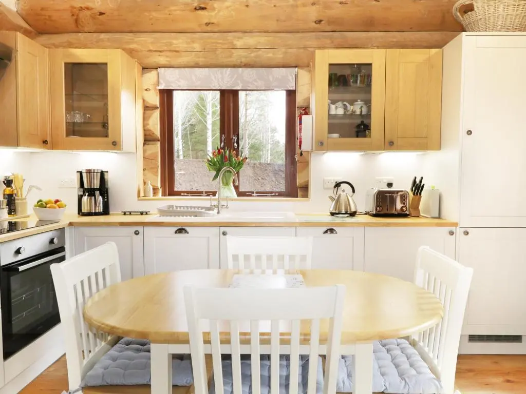a kitchen with a wooden table and white chairs at Heron Lodge in Inverness