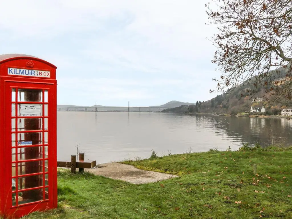 a red phone booth sitting next to a body of water at Moorhen Lodge in Inverness