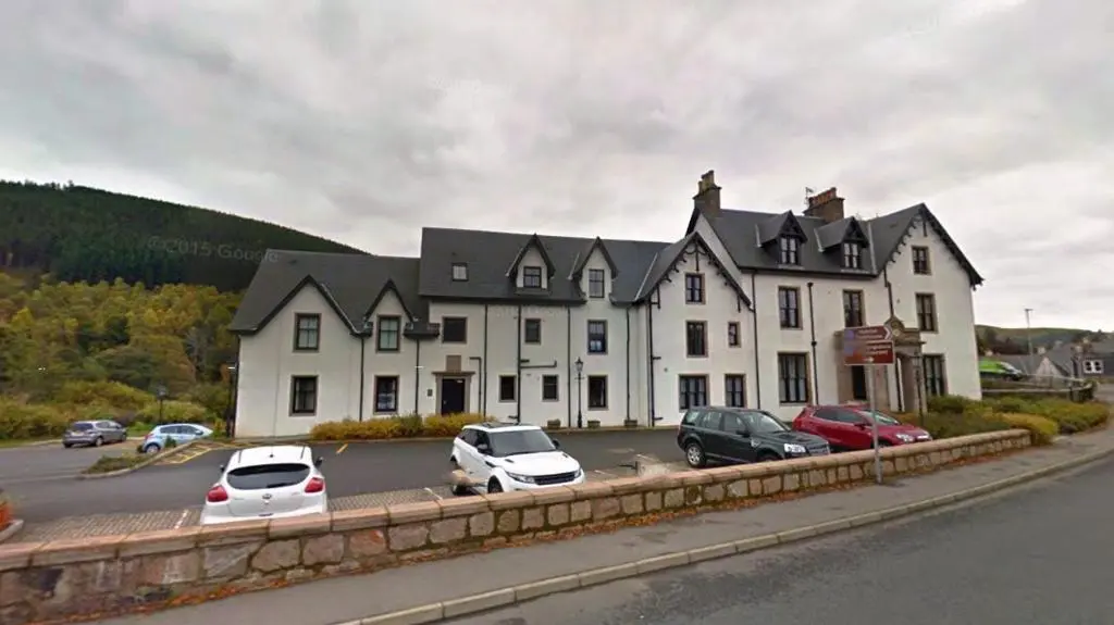 a large white building with cars parked in a parking lot at Montclaire in Ballater