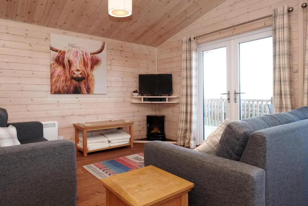 a living room with a cow painting on the wall at Burgie Woodland Lodges in Forres