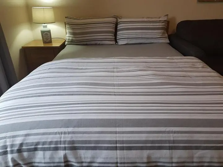 a large bed with a striped blanket on it at Yvi's 2-3 Bedroom Town Apartment in Inverurie