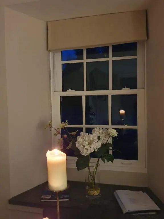 a candle and flowers on a table next to a window at Cairn Leuchan in Ballater