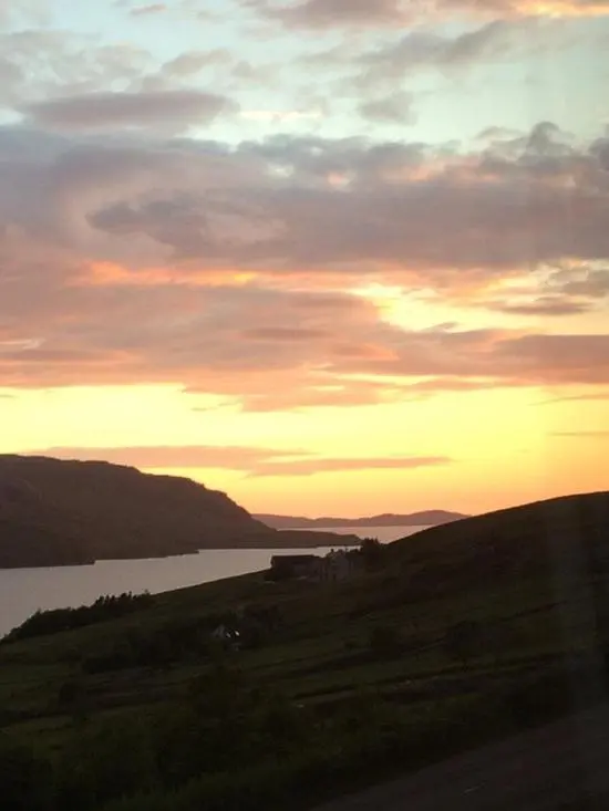 a sunset over a field with a body of water at Ardlair Guest House in Ullapool