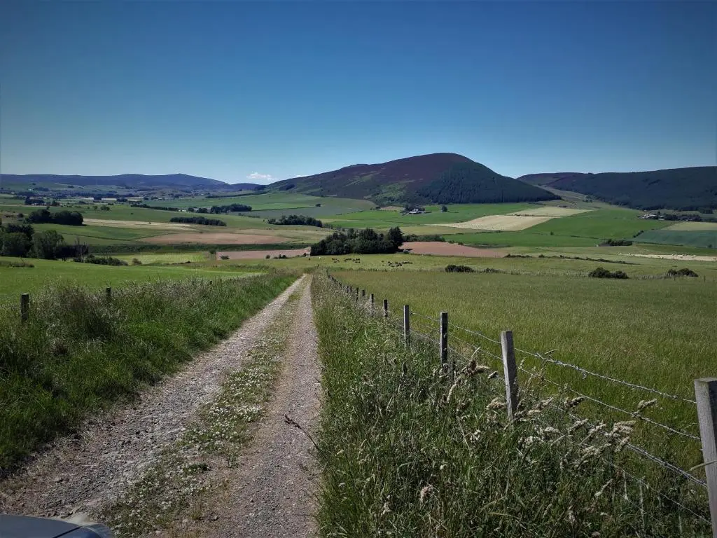 a dirt road in a field with a fence at Woodside Steading in Huntly