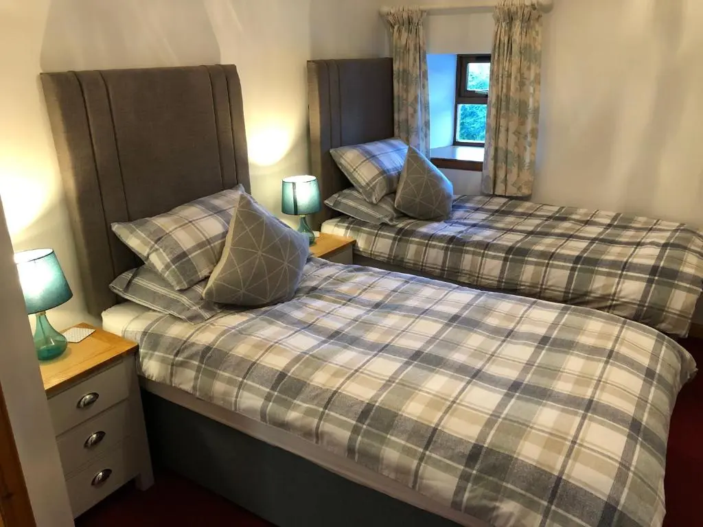 two beds in a room with two lamps and a window at Woodside Steading in Huntly
