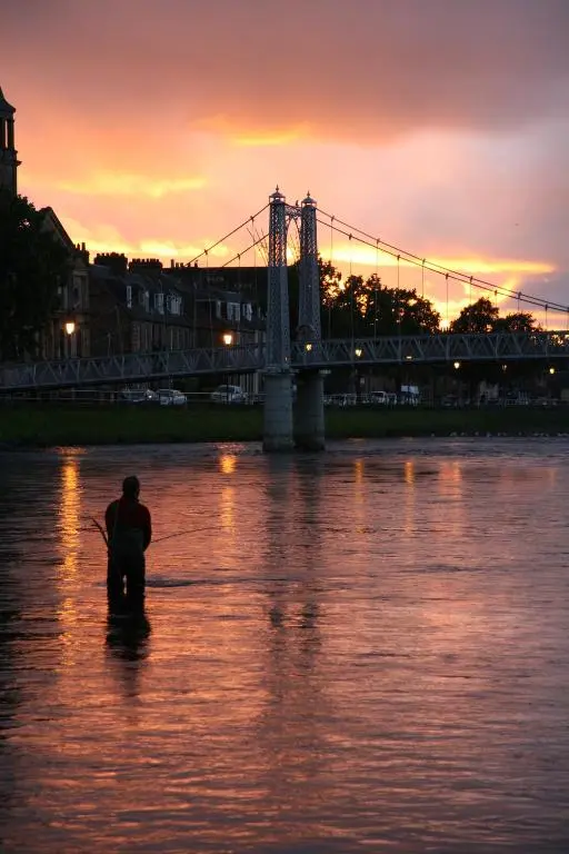 a man is standing in the water in front of a bridge at Dryburgh Apartment No3 in Inverness