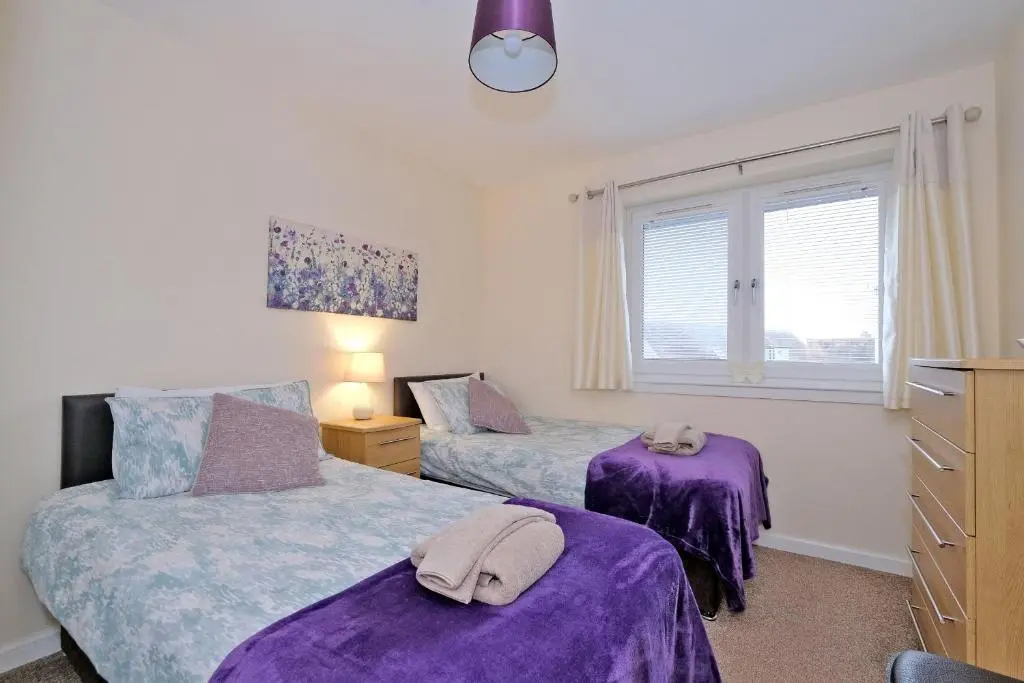 a bedroom with two beds with purple sheets and a window at Caledonia Netherhills Apartment in Aberdeen