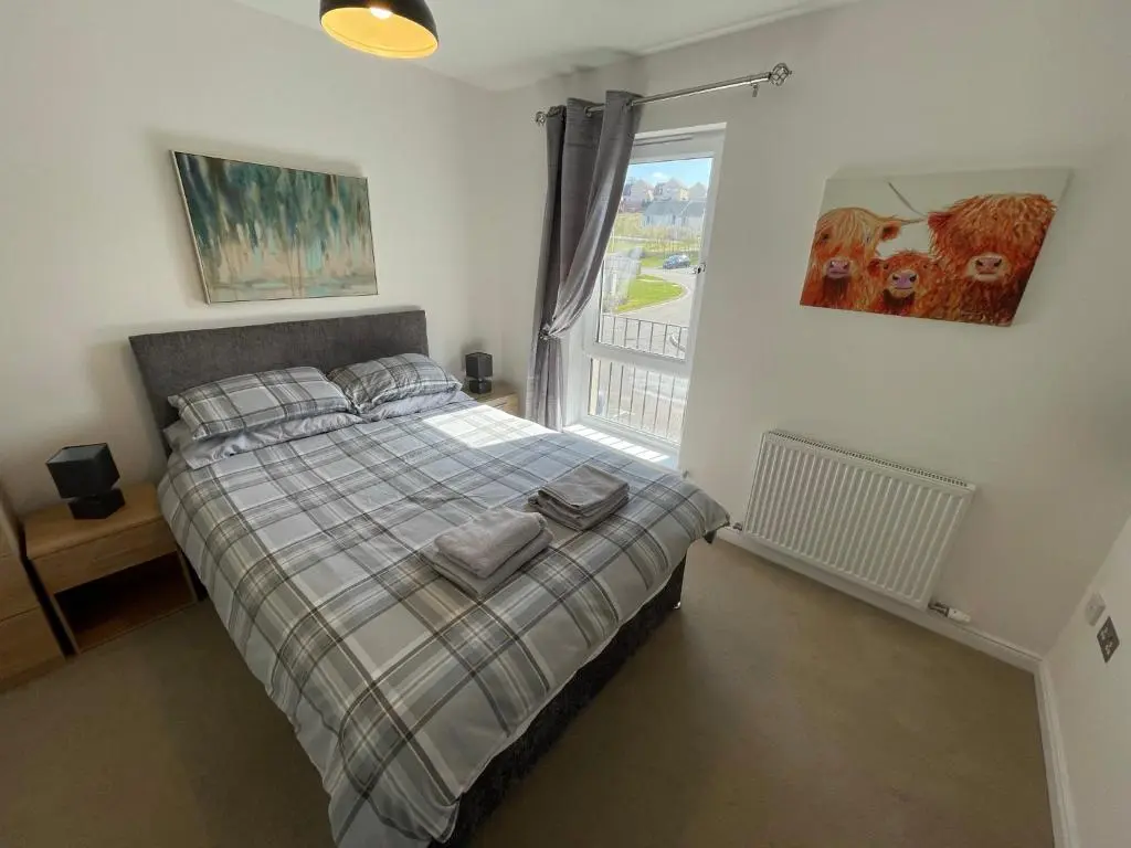 a bedroom with a bed with a plaid blanket and a window at Foxglove Apartment in Inverness