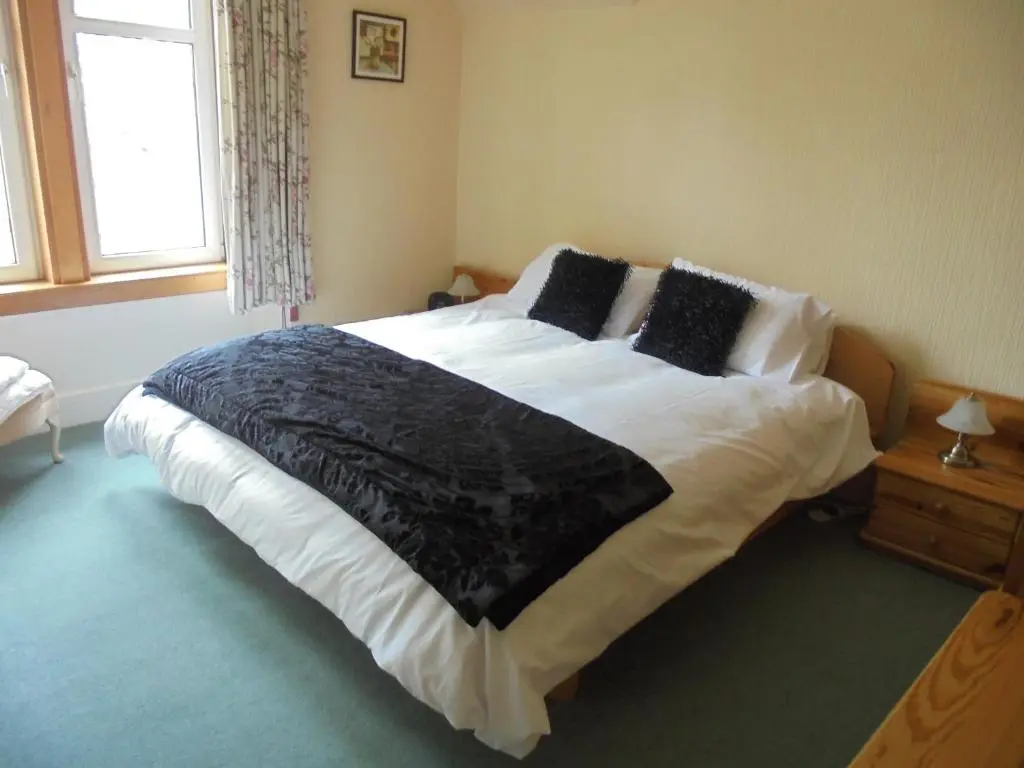 a bedroom with a large bed with black blankets and pillows at Avondale House in Kingussie