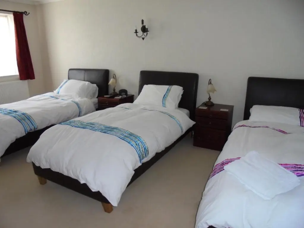 a bedroom with three beds with white sheets and a window at Avondale House in Kingussie