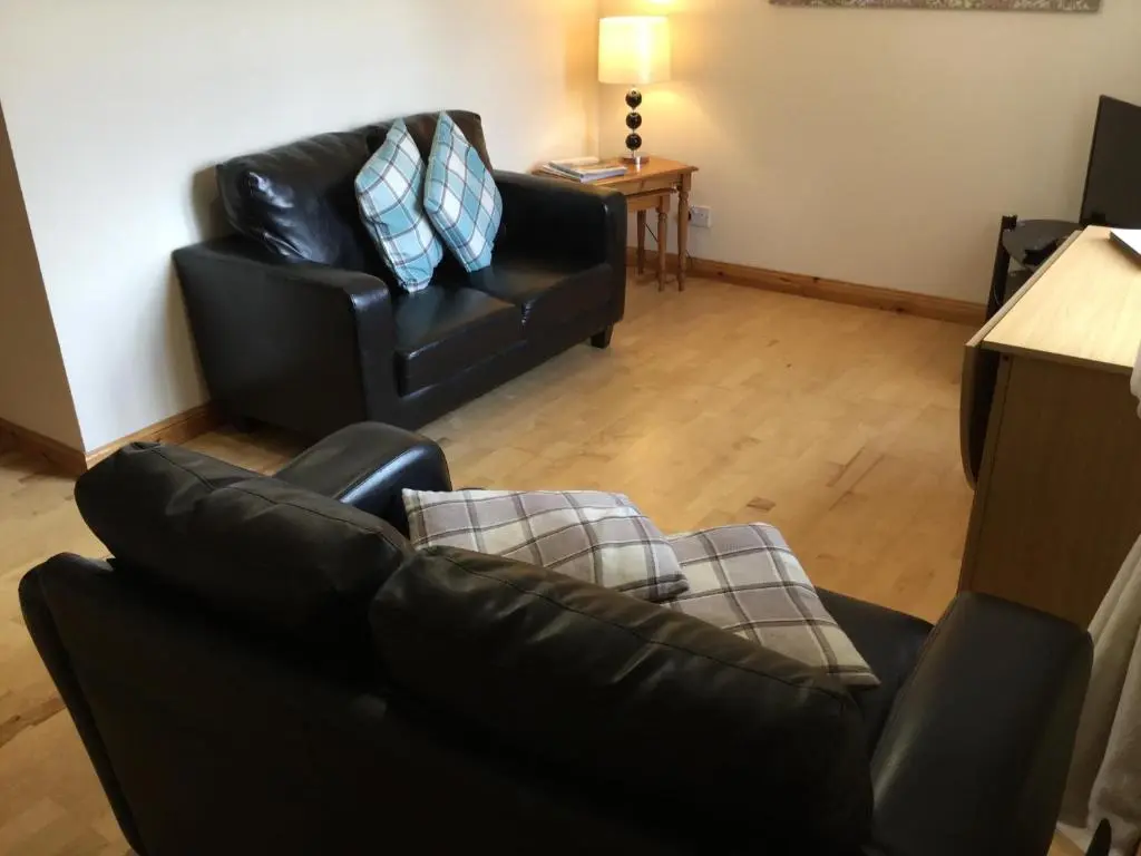 a living room with a black leather couch and a chair at Culloden Apartment Free Parking in Inverness