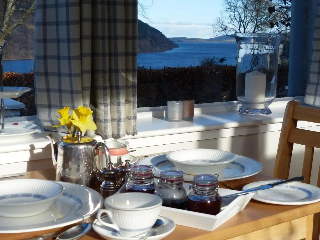 a table with plates and dishes on a table with a window at Urquhart Bay B&B in Drumnadrochit