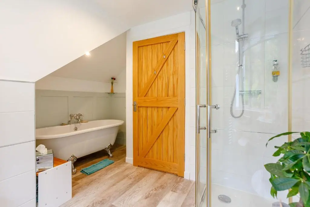 a bathroom with a wooden door and a tub and shower at Urquhart Bay B&B in Drumnadrochit