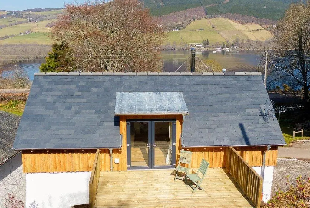 a small house with a roof on a wooden deck at Urquhart Bay Croft in Drumnadrochit