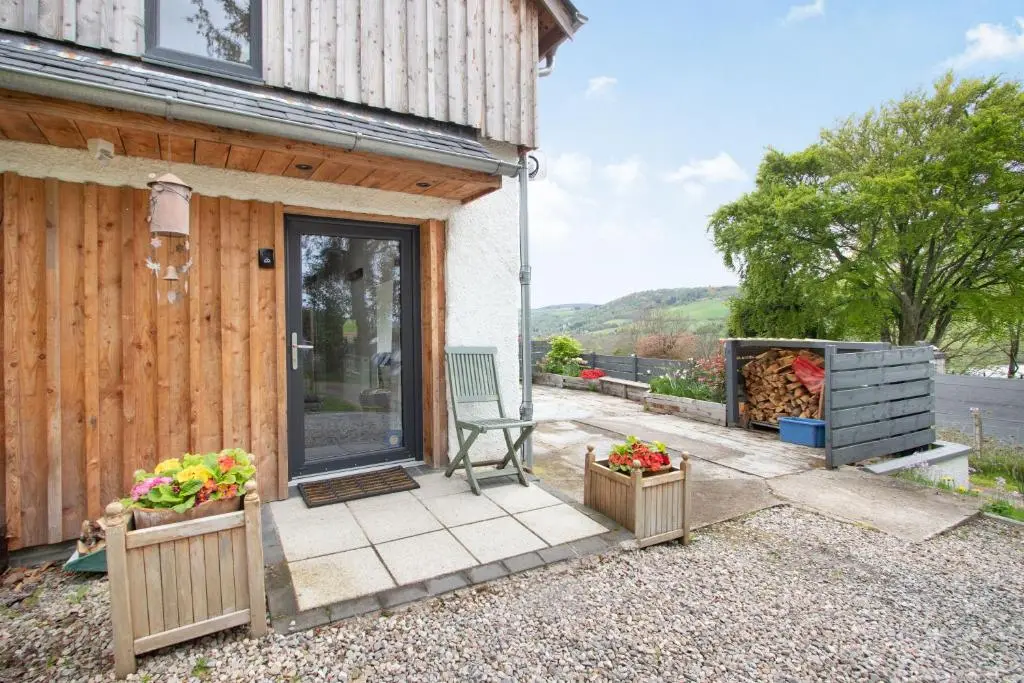 a patio of a house with a chair and flowers at Urquhart Bay Croft in Drumnadrochit