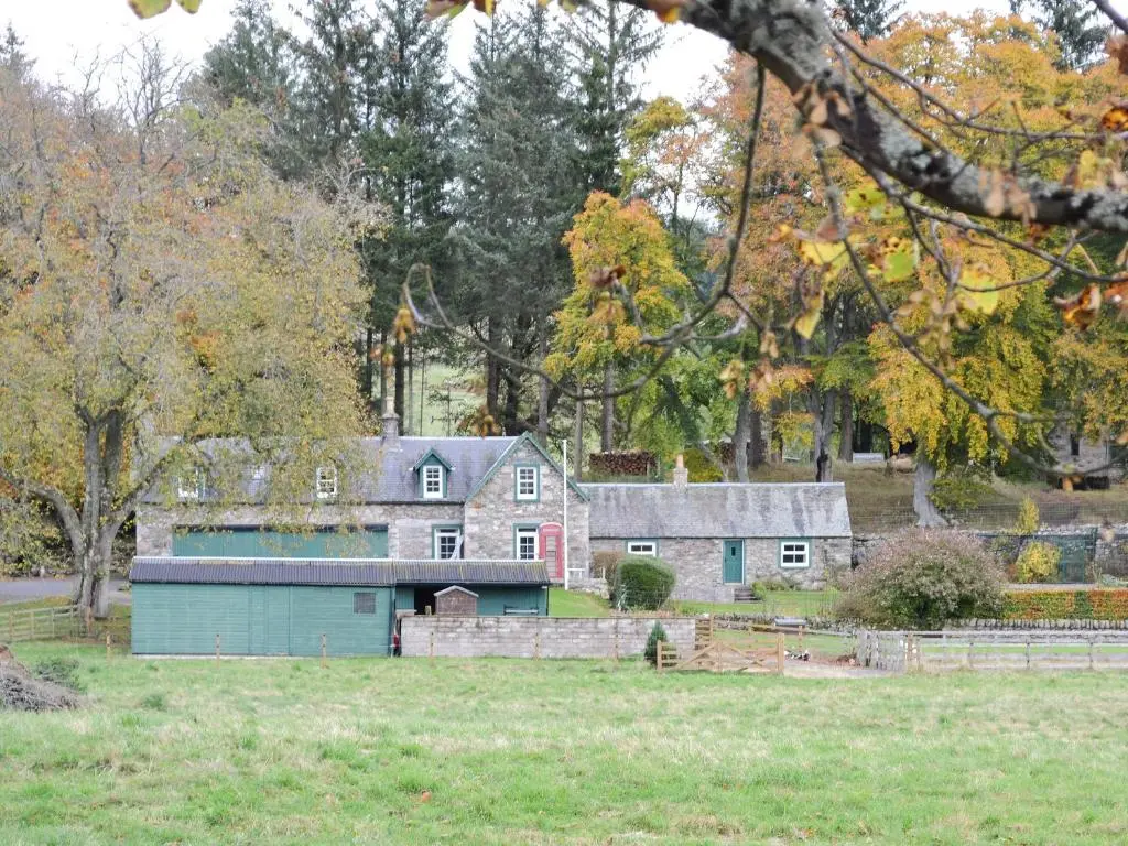 an old house with a green garage in a field at Inverchroskie Cottage in Enochdhu