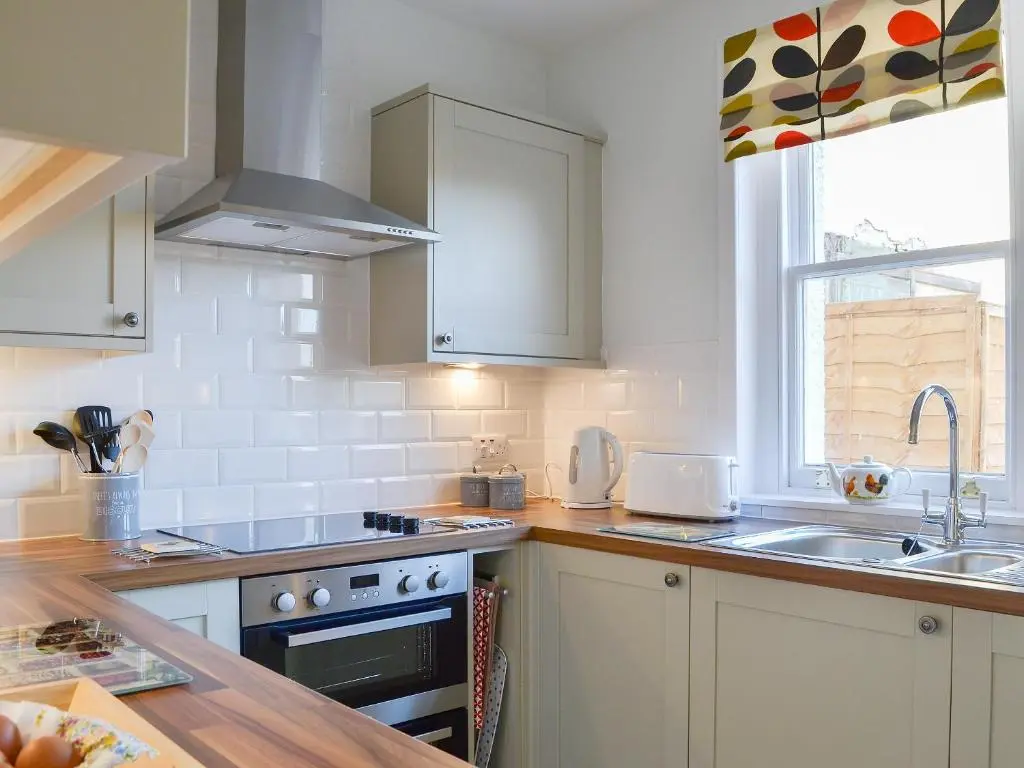 a kitchen with white cabinets and a sink and a stove at Glebe Cottage in Urray