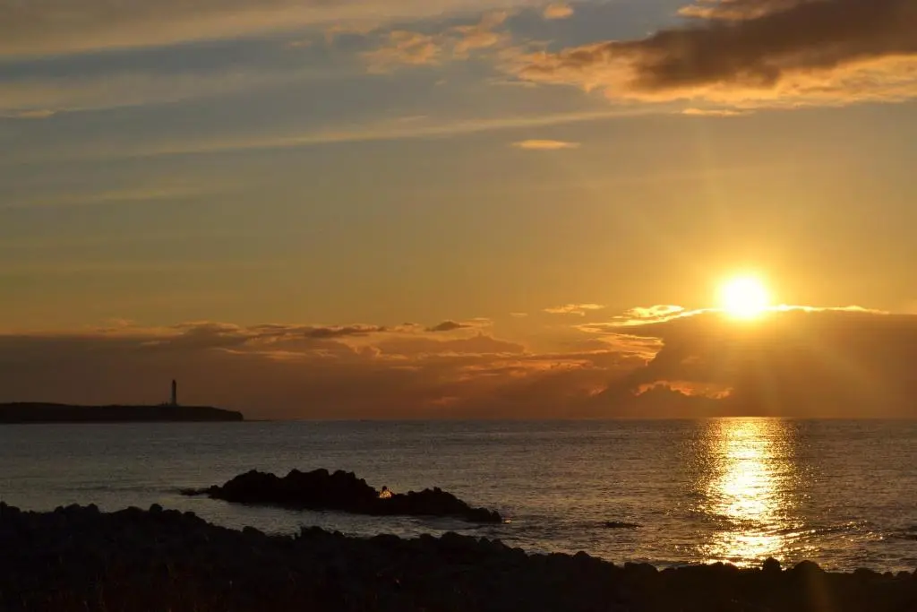 a sunset over the ocean with a lighthouse in the distance at Stotfield Hotel in Lossiemouth