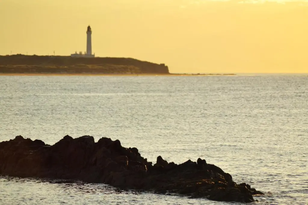a group of rocks in the water with a lighthouse in the background at Stotfield Hotel in Lossiemouth