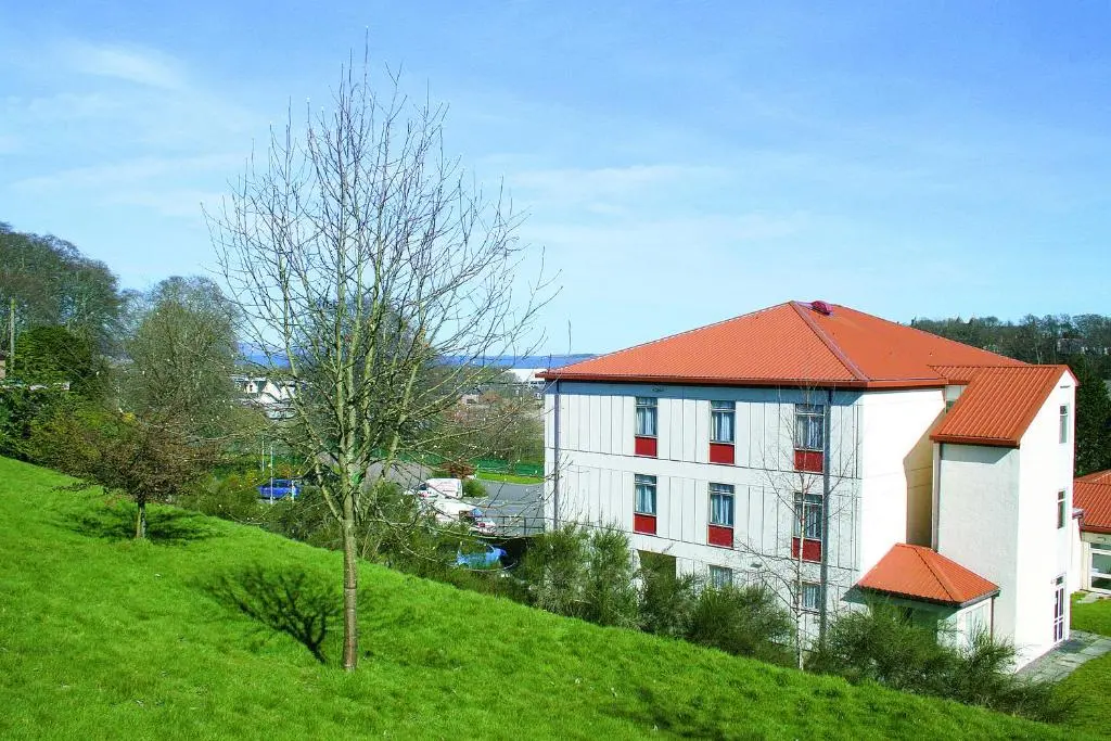 a white building with an orange roof on a green hill at Inverness Youth Hostel in Inverness