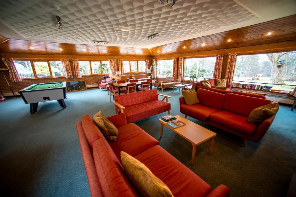 a living room with red couches and a pool table at Aviemore Youth Hostel in Aviemore