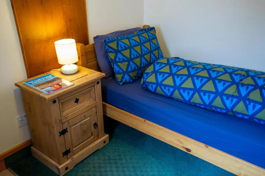 a bedroom with a blue bed with a lamp on a night stand at Aviemore Youth Hostel in Aviemore