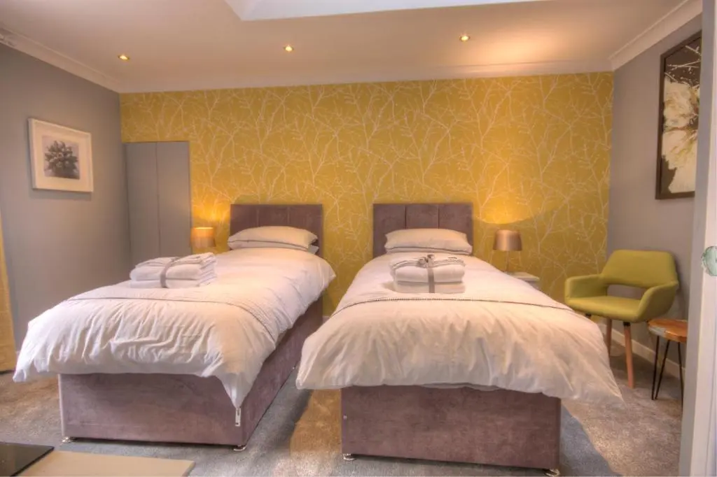 a bedroom with two beds and a green chair at Thistle Apartment Golspie in Golspie