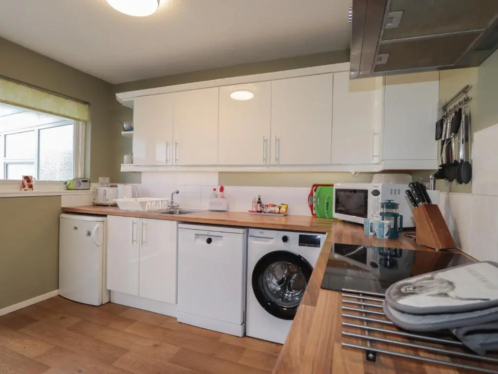 a kitchen with white cabinets and a washing machine at Steam Cottage in Aviemore