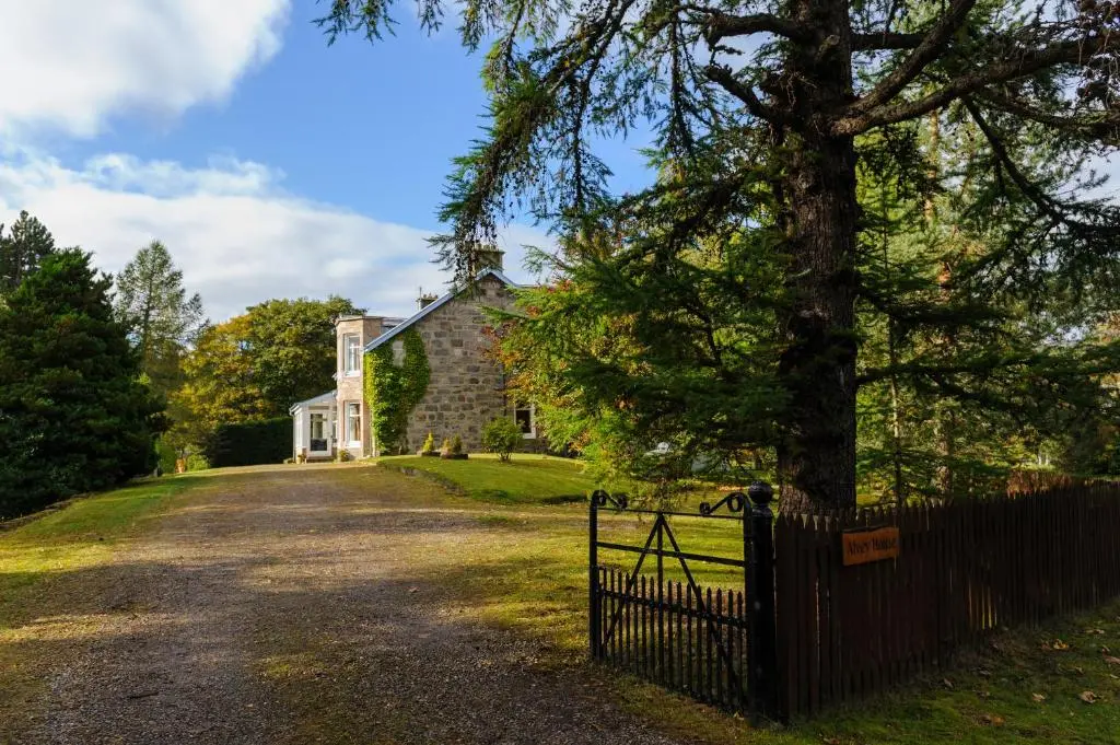 a fence in front of a house with a tree at Alvey House in Newtonmore