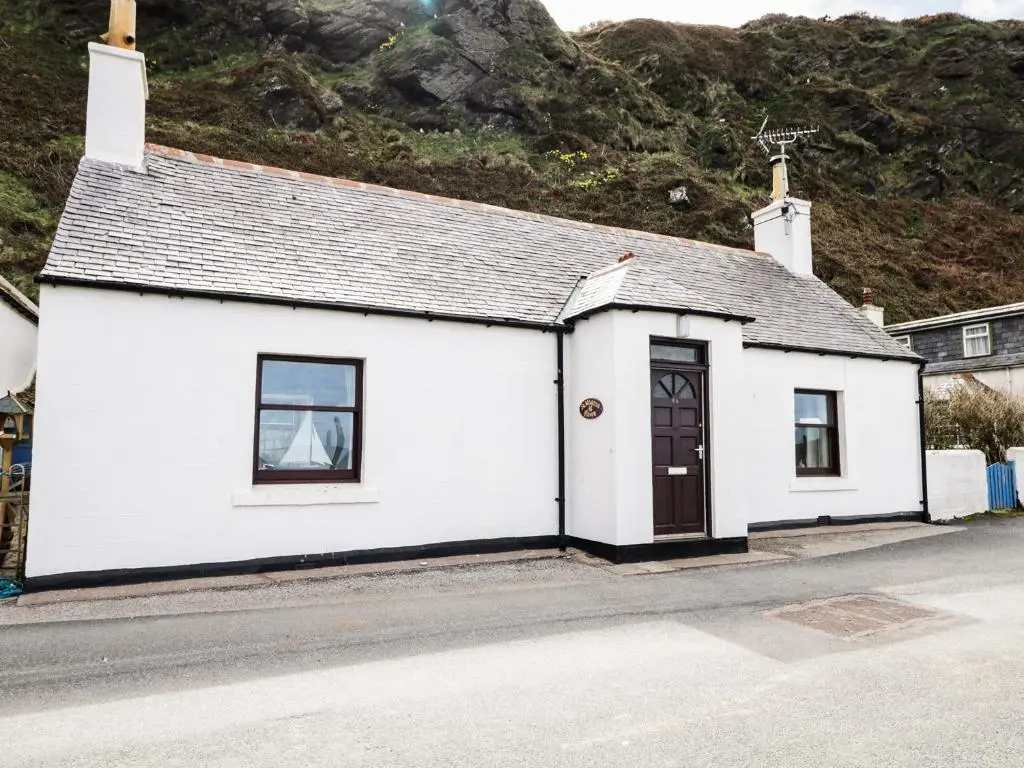 a white building with a brown door on a street at St Magnus Haven in Pennan
