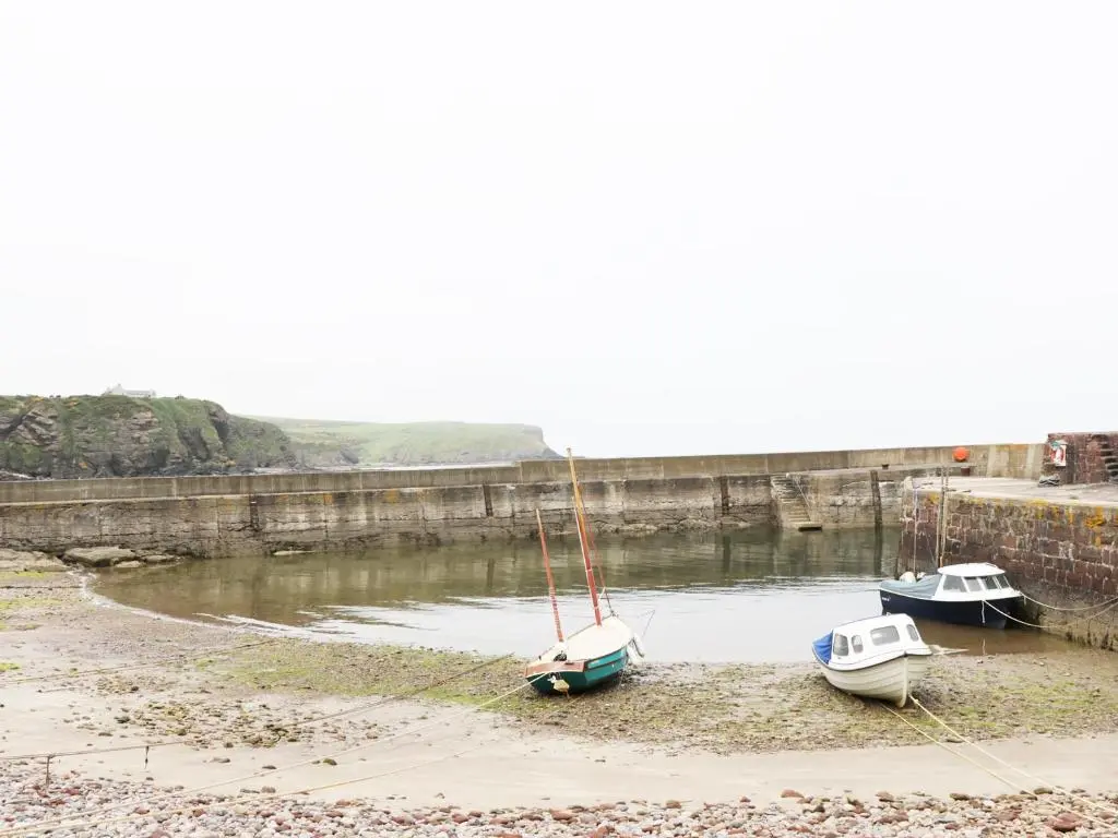 three boats sitting on the shore of a river at St Magnus Haven in Pennan