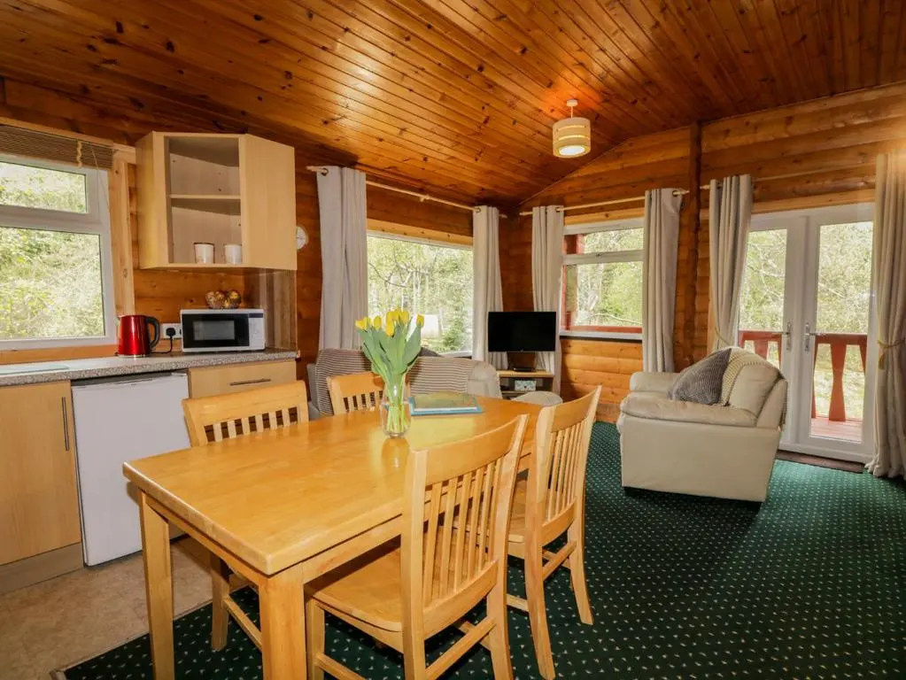 a kitchen and living room with a wooden table and chairs at Eagle Lodge in Strathpeffer