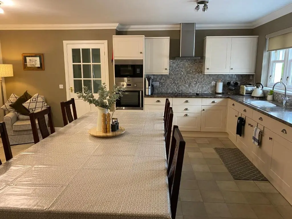 a kitchen with white cabinets and a table with chairs at Westwood Cottage in Aboyne