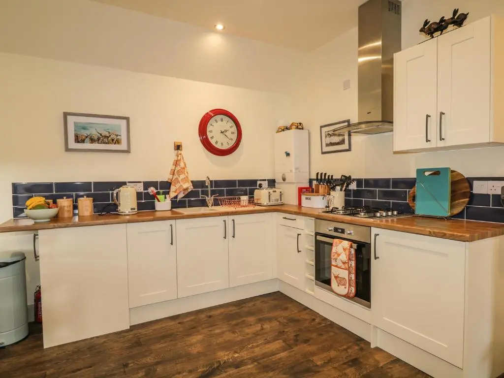a kitchen with white cabinets and a clock on the wall at East Craigdhu Cow Byre in Beauly