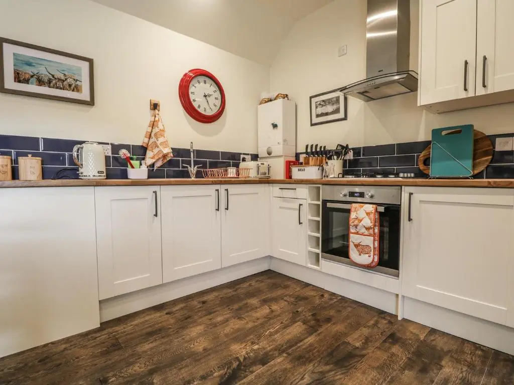 a kitchen with white cabinets and a clock on the wall at East Craigdhu Cow Byre in Beauly