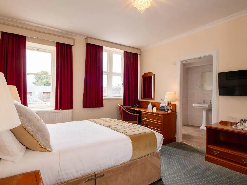 a bedroom with a large bed with red curtains at Grant Arms Hotel in Grantown on Spey