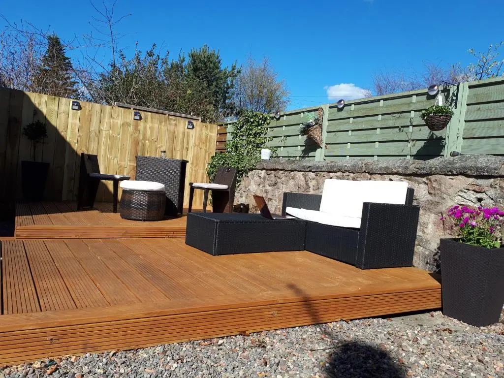 a wooden deck with two chairs and a bench on it at Fairdene Cottage in Ballater