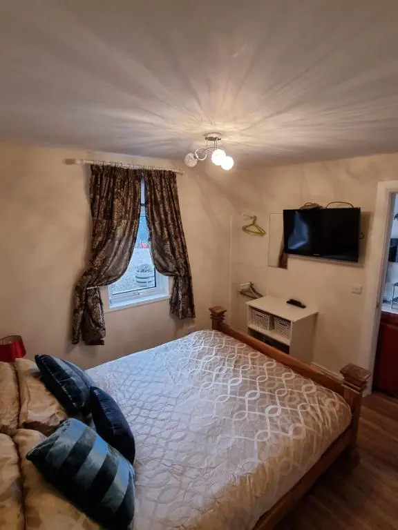 a bedroom with a bed and a television and a window at Nanny's little highland hoose in Inverness