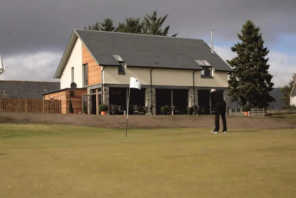 a man standing on a putting green with a flag at Macdonald Aviemore Hotel at Macdonald Aviemore Resort in Aviemore