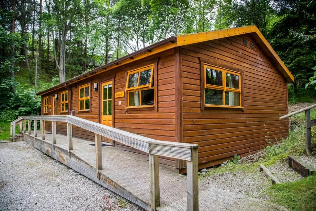 a small wooden cabin with a wooden ramp in the woods at Dulnain in Aviemore