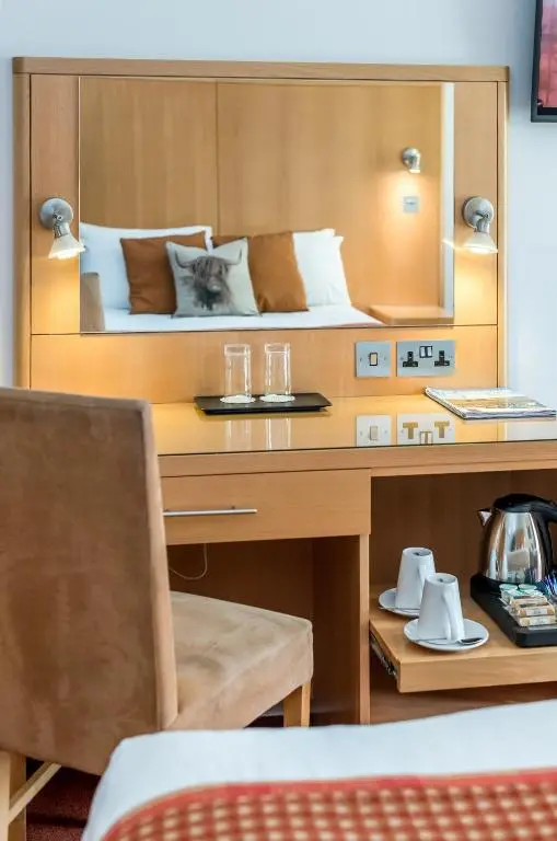 a room with a desk with a bed and a table with glasses at High Range Lodge Hotel in Aviemore