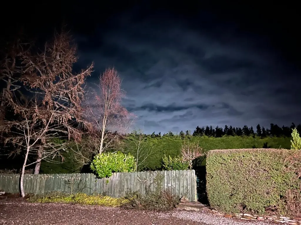 a fence and hedges in front of a dark sky at Belforte House Holiday Home in Inverness