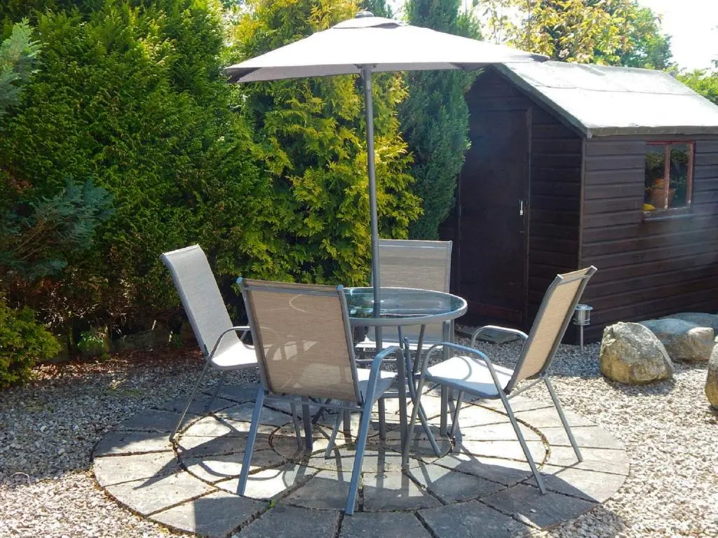 a table and chairs with an umbrella and a shed at Dalnahaven in Grantown on Spey